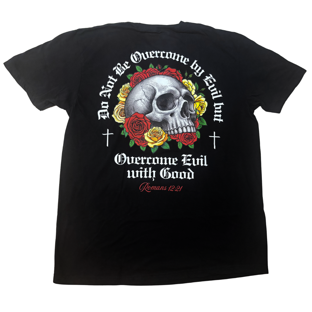 A black short-sleeve t-shirt shown from the back, featuring a large graphic print of a skull surrounded by red and yellow roses, with gothic text reading 'Do Not Be Overcome by Evil but Overcome Evil with Good' and 'Romans 12:21'.