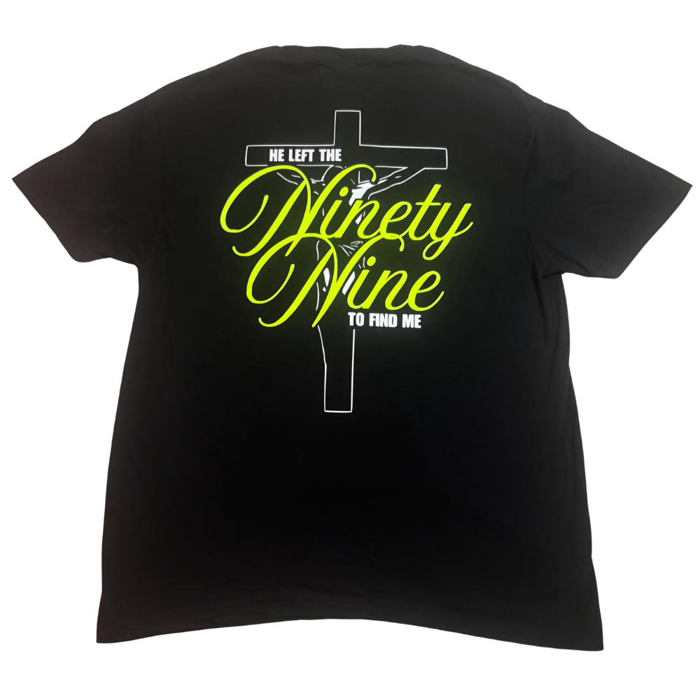 A black short-sleeve t-shirt shown from the back, featuring a graphic print of a crucifix with white line art and neon yellow puff text that says "he left the ninety nine to find me".