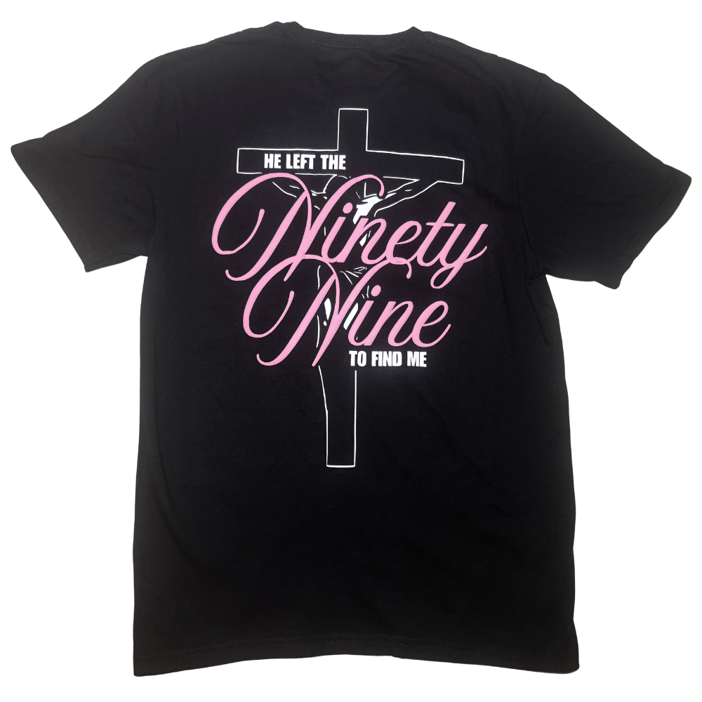 A black short-sleeve t-shirt with a graphic on the back featuring a white cross, a silhouette of Jesus, and pink script text that reads 'He left the ninety-nine to find me'.