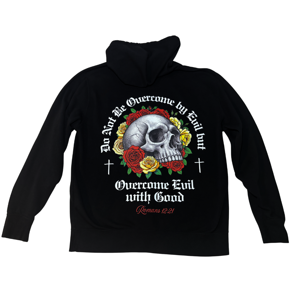 A black full-zip hoodie shown from the back, featuring a large graphic print of a skull surrounded by red and yellow roses, with white and red text reading 'Do Not Be Overcome by Evil but Overcome Evil with Good' and 'Romans 8:21'.