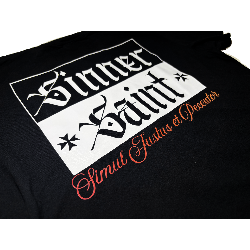 A close-up of a black graphic t-shirt featuring a white rectangular box with gothic-style text reading 'Sinner' and "Saint' and orange script text reading 'Simul Justus et Peccator' in Latin which means 'simultaneously just and sinful'