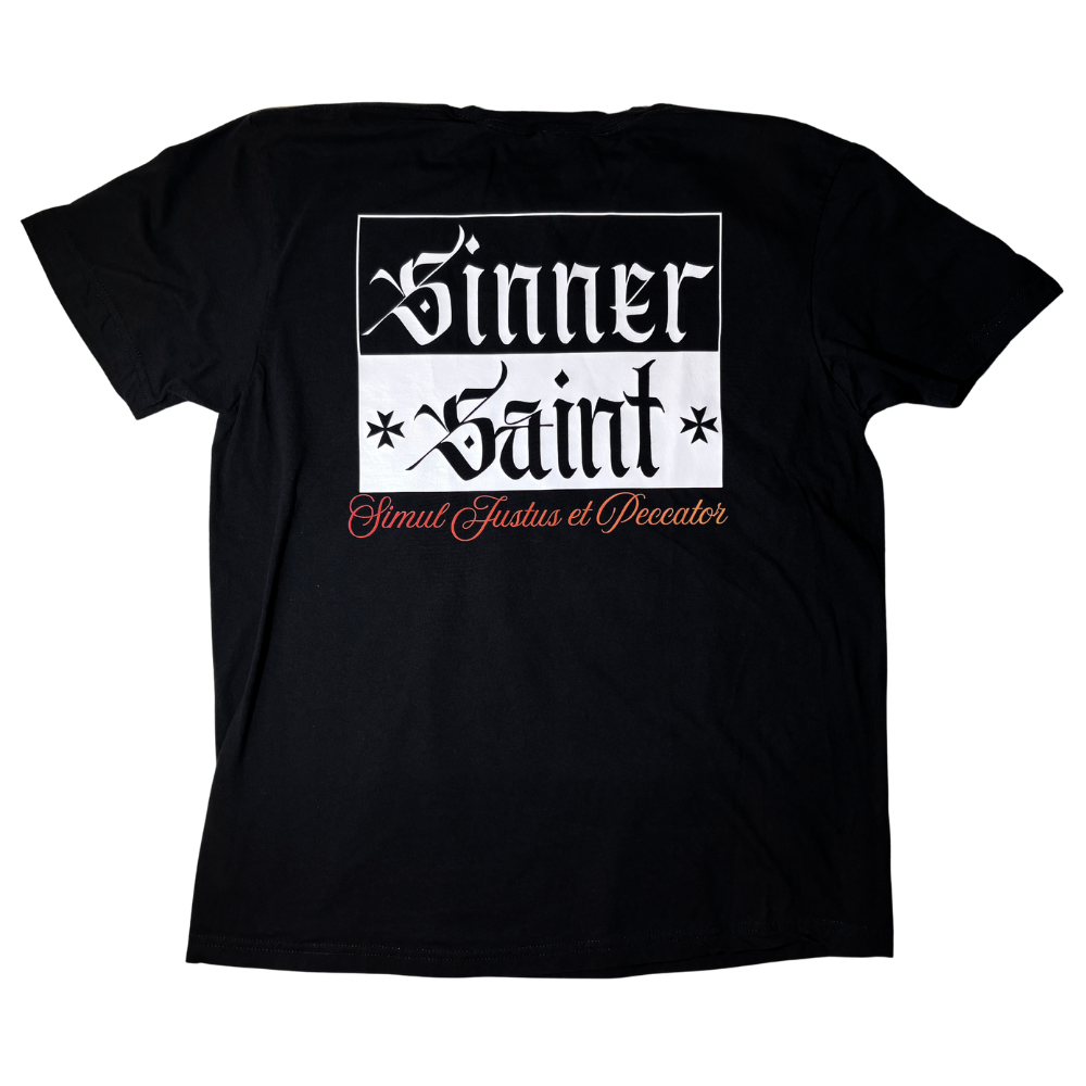 Black short sleeve shirt shown from the back that depicts oversized text white text that says 'sinner' on a black background, matching black text on a white background underneath that says 'saint', and the Latin phrase 'Simul Justus et Peccator' at the bottom of the graphic in a cursive font and red-to-orange gradient color.