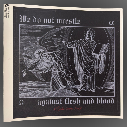 A square sticker featuring a black background with white line-art illustration of Jesus defeating Satan and text reading 'We do not wrestle against flesh and blood,' with 'Ephesians 6:12' in red script at the bottom, and the Greek 'alpha' and 'omega' letters on the outside edges.